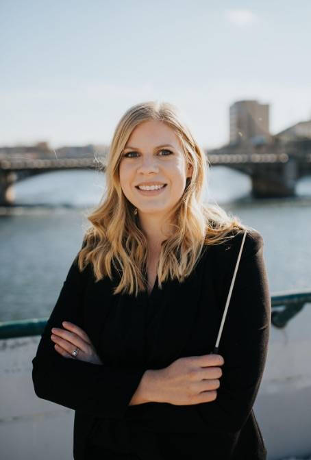 Loren Koella with conducting baton posing in front of a river